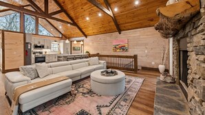 A spacious living area with a high wooden ceiling, a stone fireplace, and a large sectional sofa. - Cardinal Lodge - Elevated Luxury, Minutes From Fun (Mineral Bluff)