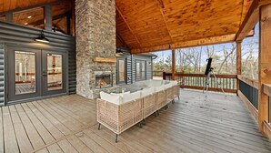 A covered outdoor area with a stone fireplace, wicker furniture, and a telescope. - Cardinal Lodge - Elevated Luxury, Minutes From Fun (Mineral Bluff)