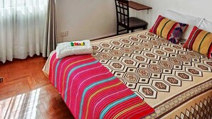 A bedroom with a patterned bedspread, a chair, and a wall-mounted painting. - Warm and cozy apartment in the heart of Cusco, Peru. (Cusco)