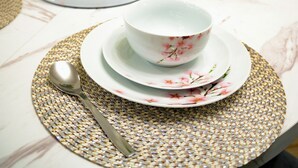 Une table à manger ornée d’un vase de fleurs blanches, d’un bol et d’une cuillère, le tout posé sur un set de table.