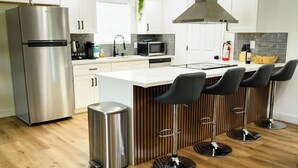 Une cuisine moderne dotée d’appareils électroménagers en acier inoxydable, d’un îlot central avec des tabourets de bar et d’un mur d’accent en bois.