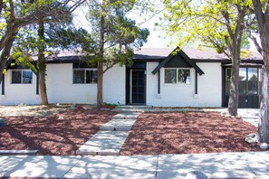 A white building with a black door and windows, surrounded by trees and a well-maintained lawn.