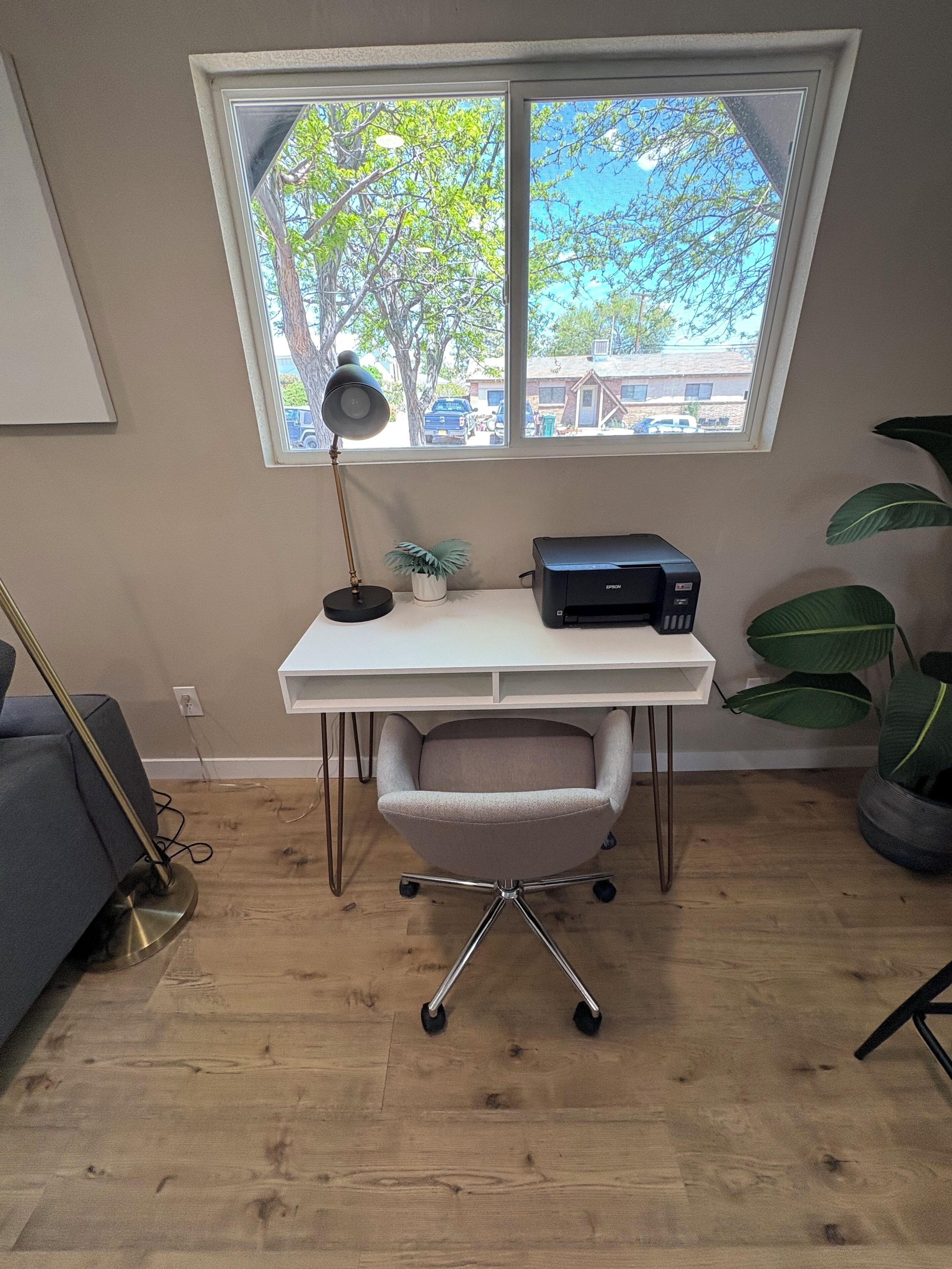 A workspace with a desk, chair, printer, lamp, and potted plants.