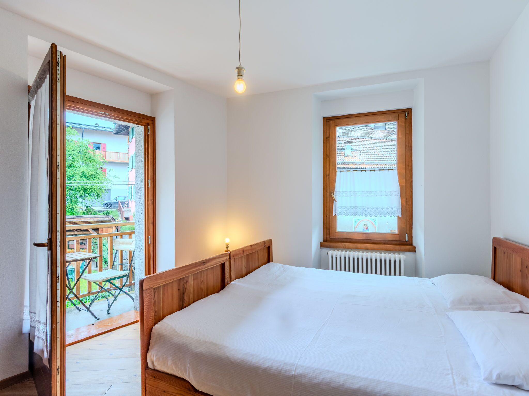A bedroom with a wooden bed, a window with a view of buildings, and a door leading to an outdoor area.