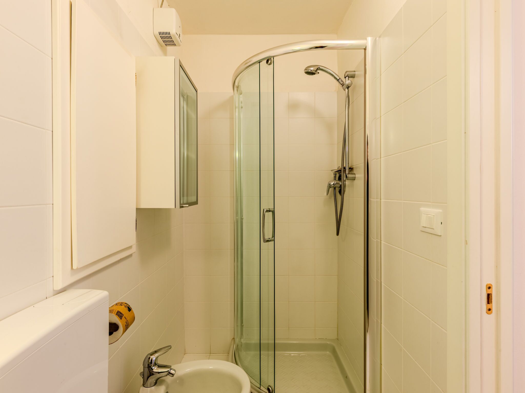 Ein kleines Badezimmer mit Duschkabine aus Glas, einem weißen Waschbecken und einer Toilette.