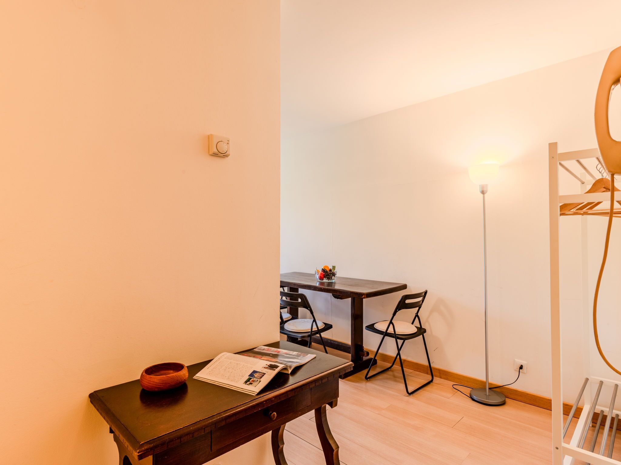 Une petite pièce comprenant un bureau en bois, une chaise, une table et un lampadaire.