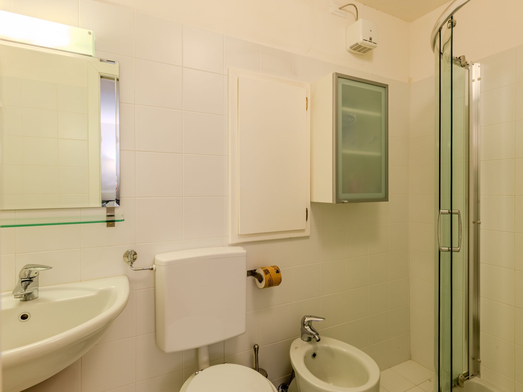 Baño con inodoro, bidé, lavabo, cabina de ducha de vidrio y espejo.