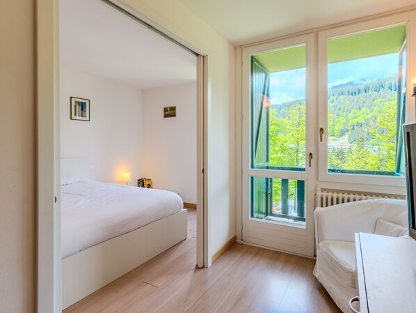 A bedroom with a bed, a bedside table with books, a window with a view of trees, and a radiator.