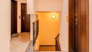 Un pasillo con una puerta de madera a la derecha, una lámpara en la pared y piso alfombrado.