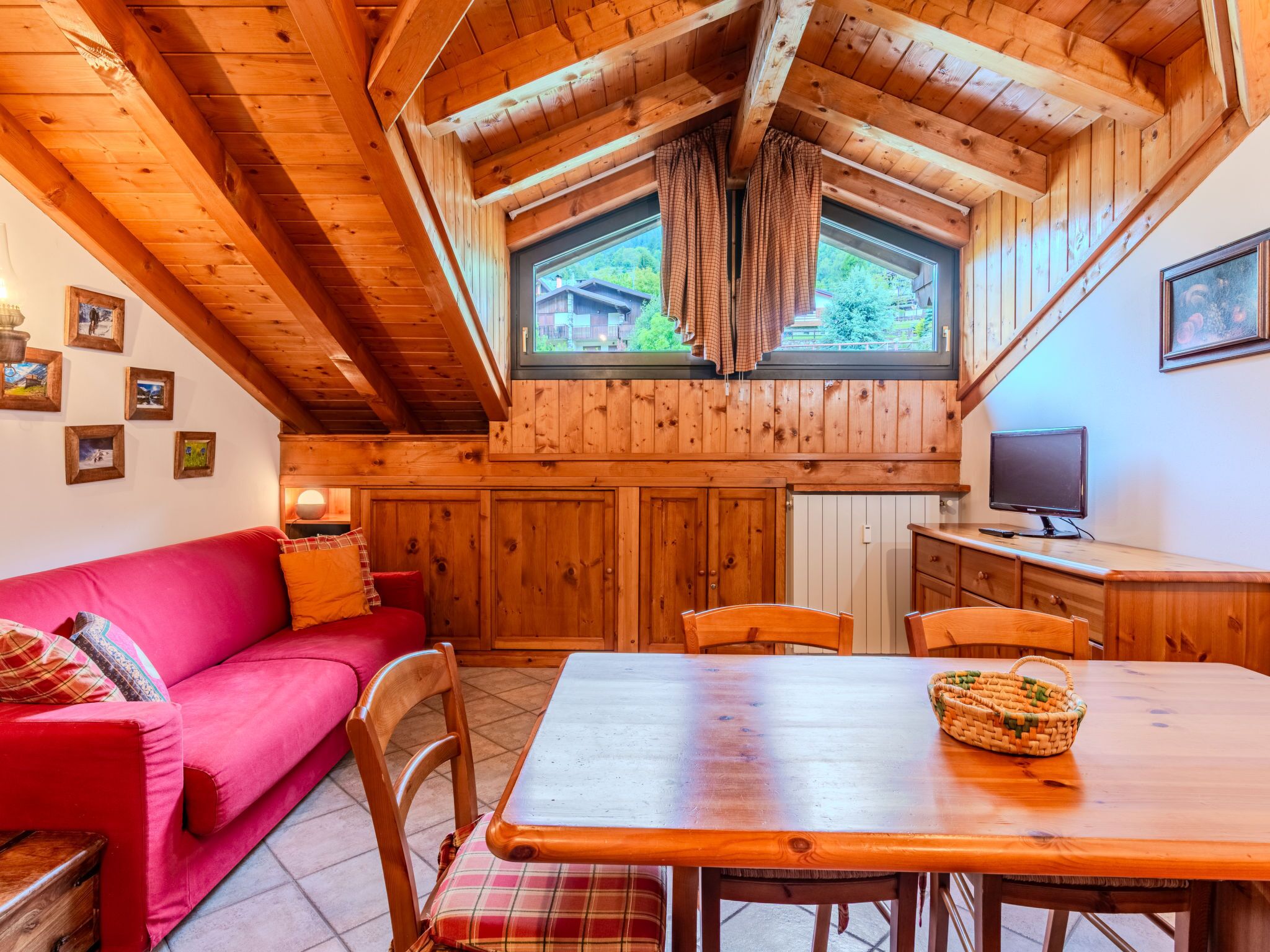 L’intérieur d’un chalet accueillant, avec un plafond en bois, un canapé rouge, une table à manger et un téléviseur.