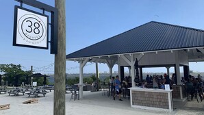 Ein Restaurant direkt am Strand mit Außenbestuhlung, einem überdachten Pavillon und einem Schild, das eine Temperatur von 38 Grad anzeigt.