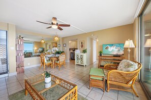 A spacious living area with a dining table, wicker furniture, a ceiling fan, and a television.