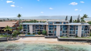 Un hôtel situé en bord de mer, avec plusieurs étages, une piscine et une vue sur l’océan et les montagnes lointaines.