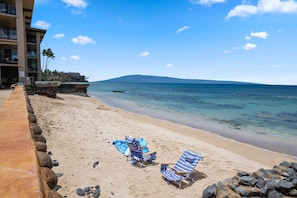 A beach with two striped beach chairs, a wooden boardwalk, and a building with balconies overlooking the ocean.