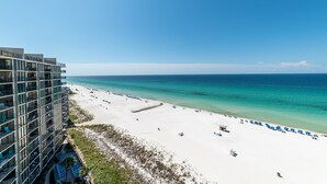 Un hôtel situé en bord de mer, doté d’une plage de sable blanc, d’une eau turquoise cristalline et d’un bâtiment moderne avec des balcons.