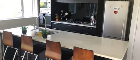 A modern kitchen with a central island, bar stools, a stainless steel refrigerator, and a window providing natural light.