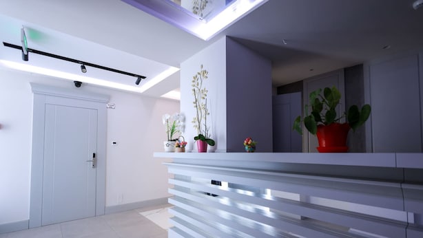 A modern reception area with a white reception desk, potted plants, and a security camera. - Grandstay Beach Room 01 (Durrës)