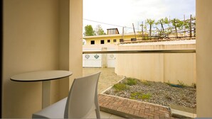 A view from a balcony with a table and chair, a garden area with plants, and a building with a yellow facade in the background. - Grandstay Beach Room 01 (Durrës)