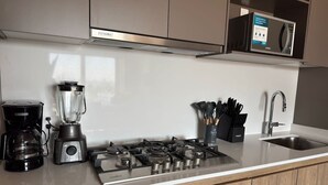 Eine Küche mit Gaskochfeld, Kaffeemaschine, Mixer und Mikrowelle auf einer weißen Arbeitsplatte.