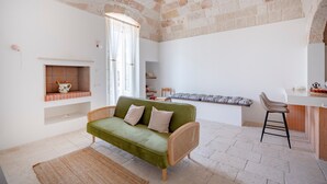 A cozy living area with a green sofa, a wooden chair, a fireplace, and a kitchen area with a bench. - Apartment 'Lemos' with Private Terrace, Wi-Fi and Air Conditioning (Triggianello)
