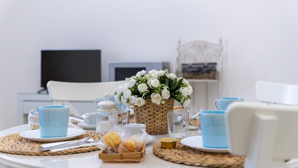 Una mesa de desayuno con un protector de tela trenzado, un cesto de flores blancas y una taza azul.