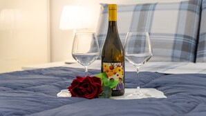 Una cama con una manta azul, una botella de vino, dos copas de vino y una rosa roja.