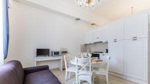 Una cocina moderna con armarios blancos, una mesa de comedor con sillas, un televisor de pantalla plana y un sofá en la sala de estar.