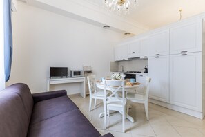 Une cuisine moderne avec des meubles blancs, une table à manger avec des chaises, un téléviseur à écran plat et un canapé dans l’espace salon.