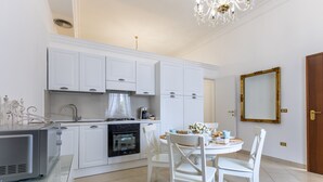 Una cocina moderna con muebles blancos, una mesa de comedor con sillas, una araña y un espejo grande en la pared.