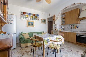 A compact kitchen with a dining table, wooden cabinets, a refrigerator, and a tiled backsplash. - Holiday Home 'Al Castello' with Private Terrace, Wi-Fi and Air Conditioning (Ficarazzi)