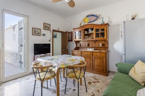 A dining area with a table and chairs, a wooden cabinet with glass doors, a television, and a green sofa. - Holiday Home 'Al Castello' with Private Terrace, Wi-Fi and Air Conditioning (Ficarazzi)