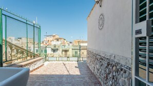 A rooftop terrace with a stone wall, a metal fence, and a view of buildings in the background. - Holiday Home 'Al Castello' with Private Terrace, Wi-Fi and Air Conditioning (Ficarazzi)