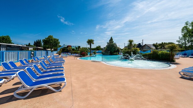 Área de piscina com espreguiçadeiras azuis, um recurso aquático e céu azul límpido.