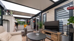 Um espaço moderno para atividades ao ar livre, com um sofá, cadeiras, uma TV e uma mesa.