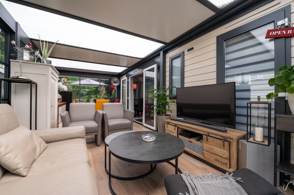 A modern outdoor living space with a sofa, chairs, a TV, and a table.