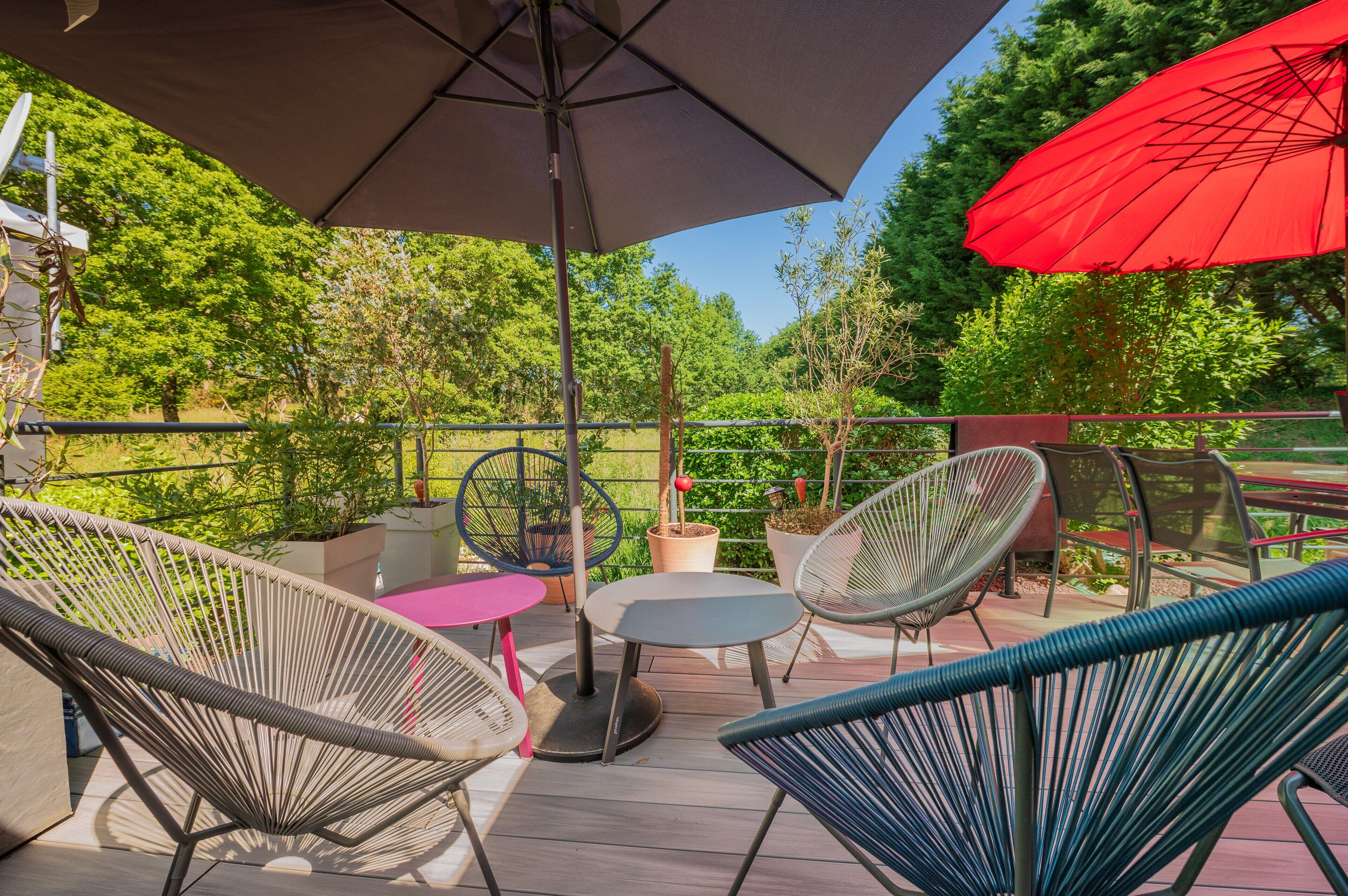 Eine Terrasse mit Korbstühlen, einem Tisch und einem roten Sonnenschirm.