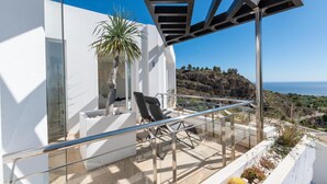 A modern balcony with a glass railing, a chair, and a potted plant.