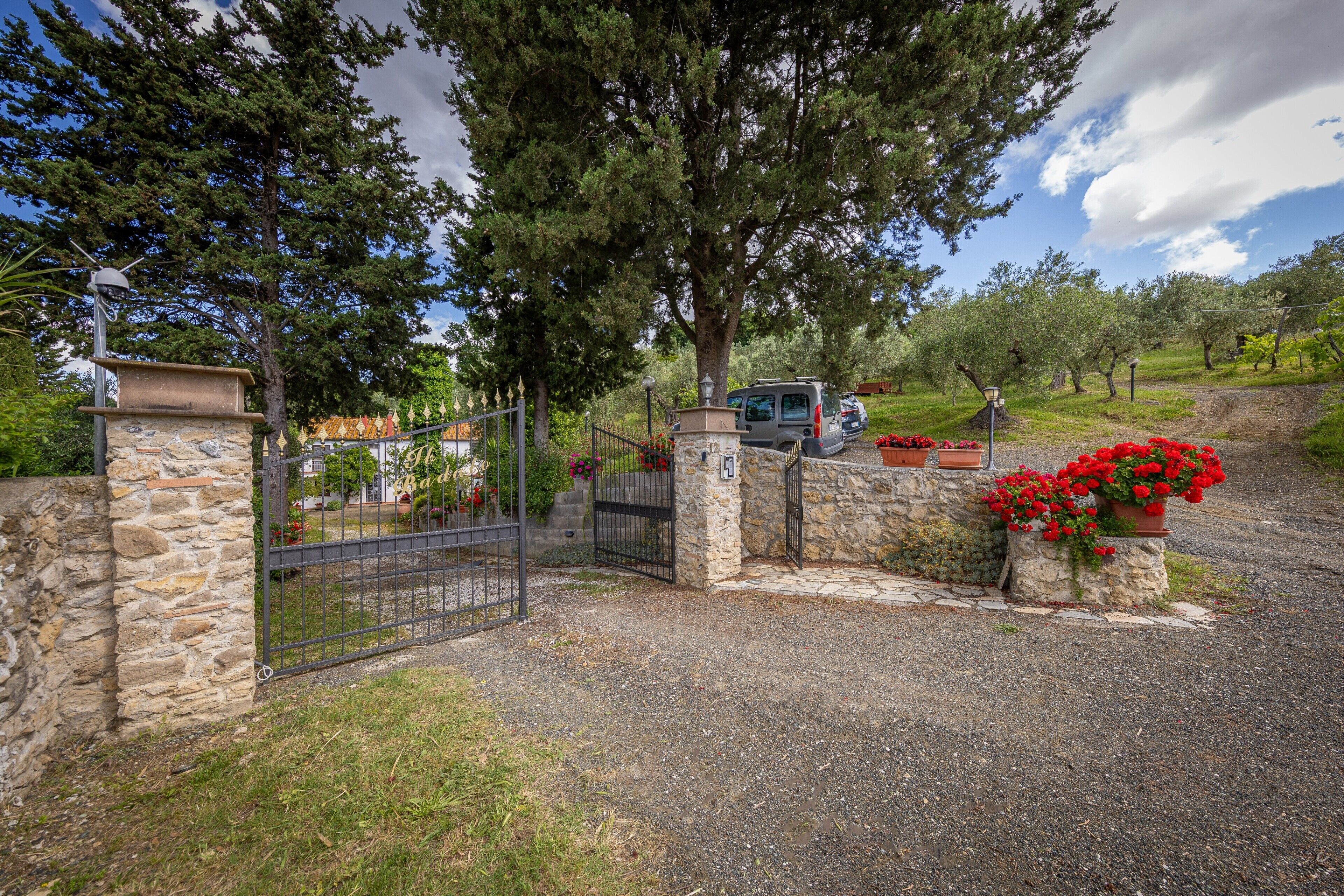 A gated entrance with stone walls, a gravel path, and red flowers.