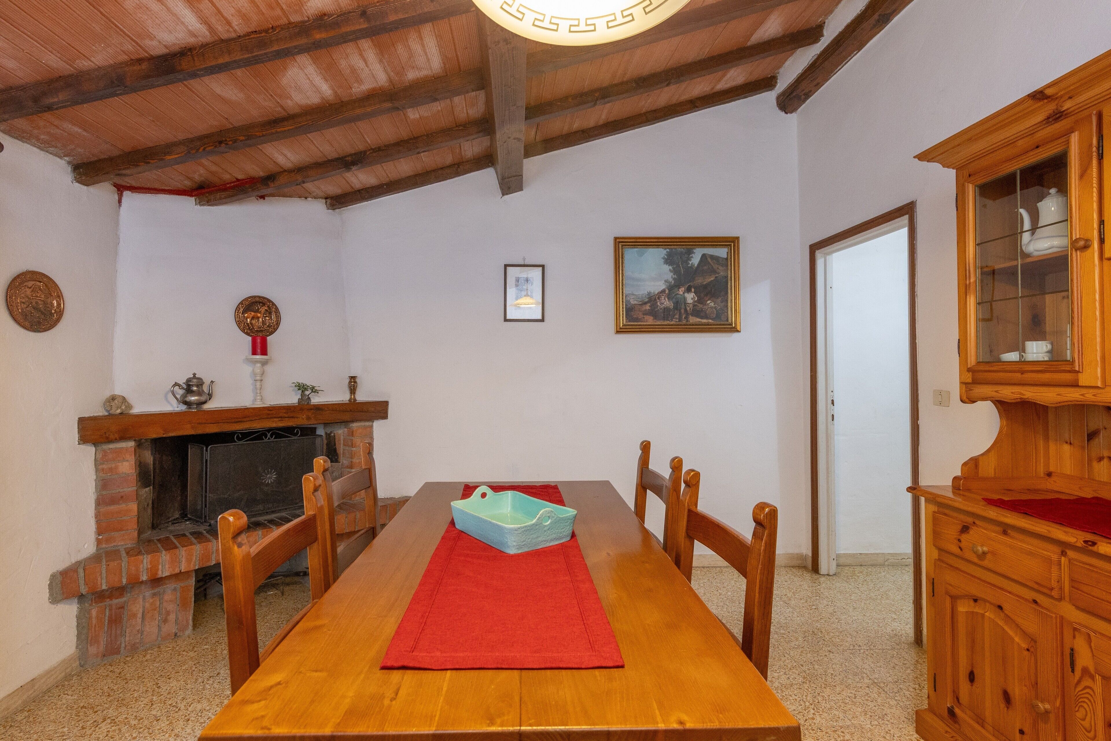 Comedor con mesa y sillas de madera, chimenea, aparador de madera y un cuadro en la pared.