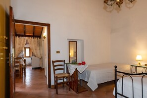 Une chambre à coucher avec un lit, une chaise, une table ornée d’un vase de fleurs, une lampe et un miroir.
