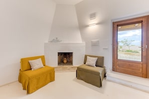 A room with a fireplace, two sofas, a wooden door, and a view of the beach.