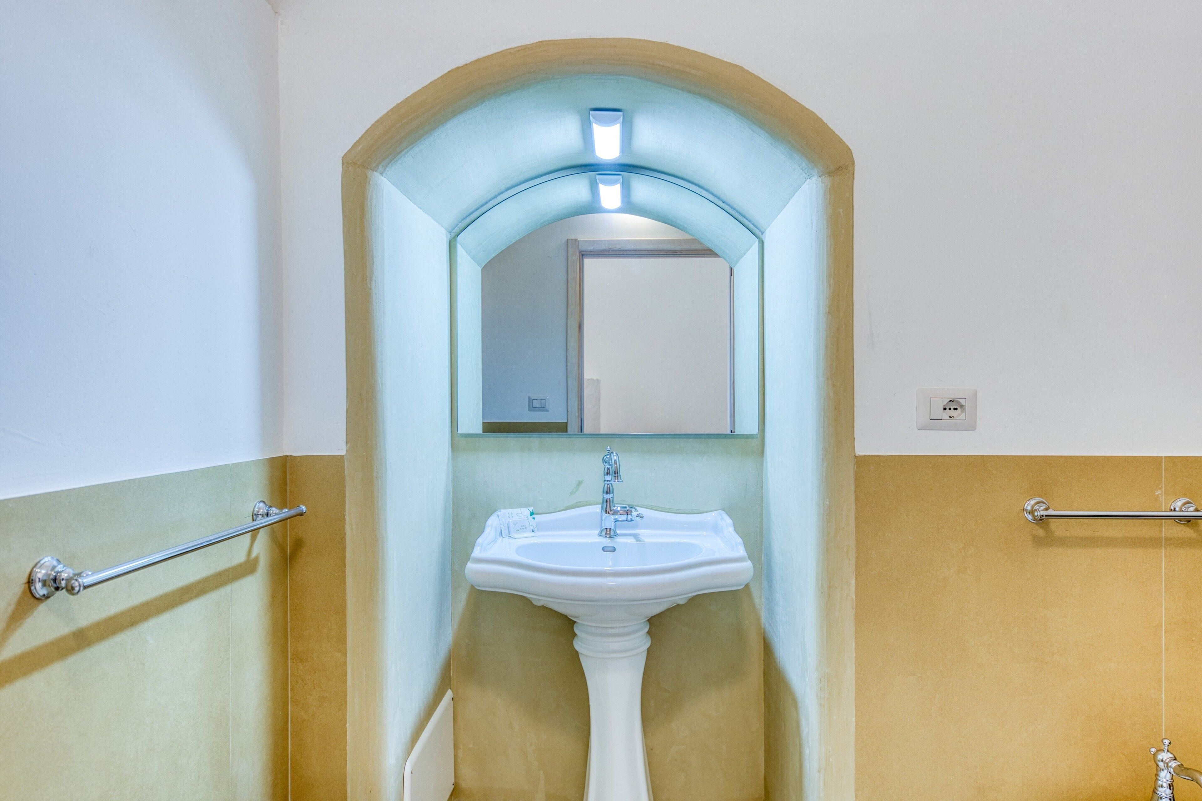 A bathroom with a white pedestal sink, a mirror above it, and a towel rack on the wall.