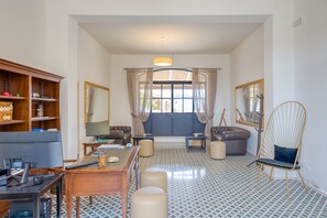 Una sala de estar con escritorio, computadora, sofá, otomanes y una silla.
