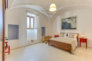 Un dormitorio con una cama grande, una ventana con cortinas, un cuadro colgado en la pared y una mesita de noche con lámpara.