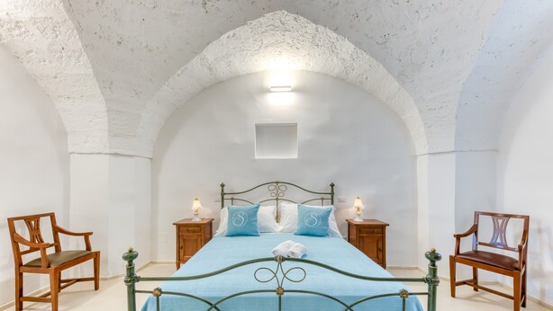 Une chambre à coucher comprenant un lit, deux tables de chevet, deux chaises en bois et un plafond blanc orné d’un motif en arc.