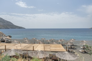 A beachside area with umbrellas and chairs, a clear view of the sea, and a rocky hillside in the background. - Apartment 'No 5' with sea view, Wi-Fi and air conditioning (Kalymnos)