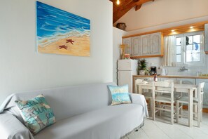 Une pièce comprenant un canapé, un tableau représentant une scène de plage, une table à manger avec des chaises et un coin cuisine.
