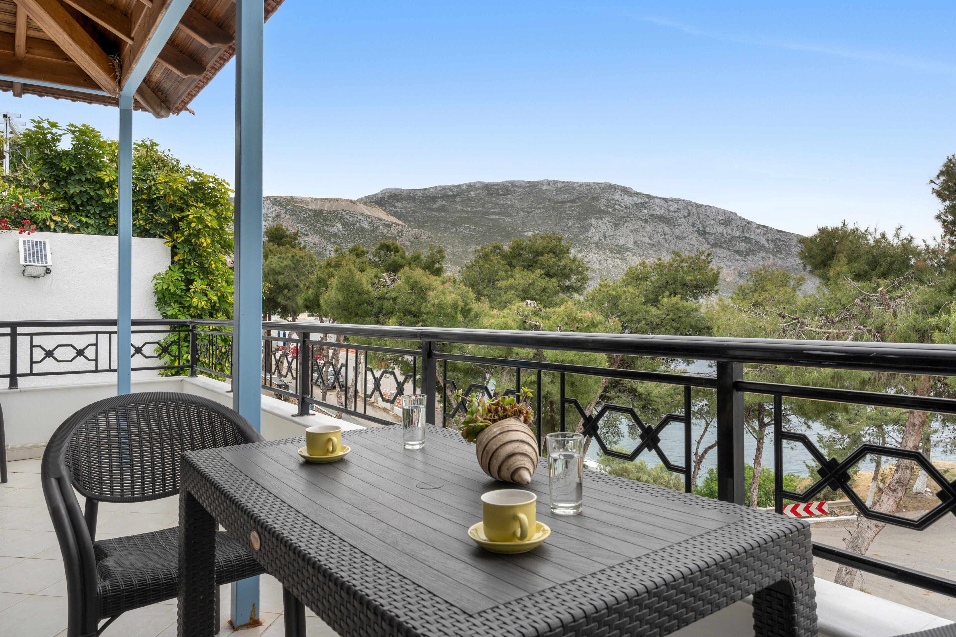 A balcony with wicker furniture, a table with cups and a vase, and a view of a mountain and trees.