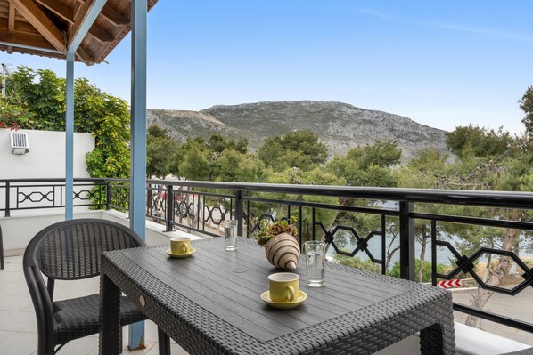 A balcony with wicker furniture, a table with cups and a vase, and a view of a mountain and trees.