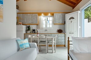 A compact kitchen with white cabinets, a dining table, and a sofa with a beach-themed pillow. - Apartment 'No 5' with sea view, Wi-Fi and air conditioning (Kalymnos)